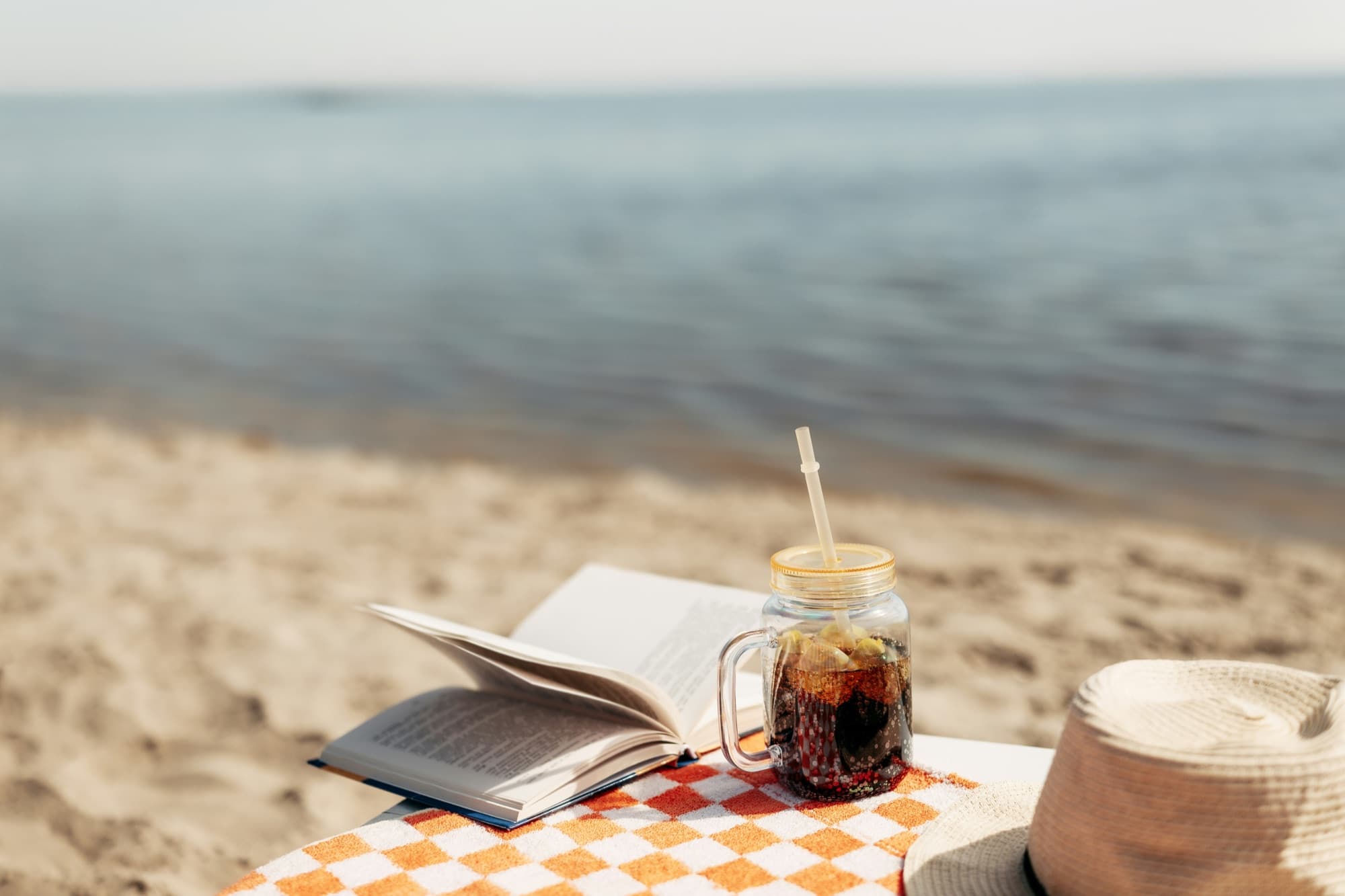 An open book and an iced drink on a sandy beach